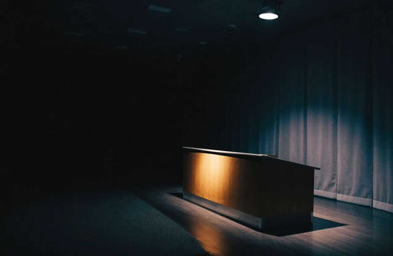An empty congressional hearing room at night with one lamp left on over the long table