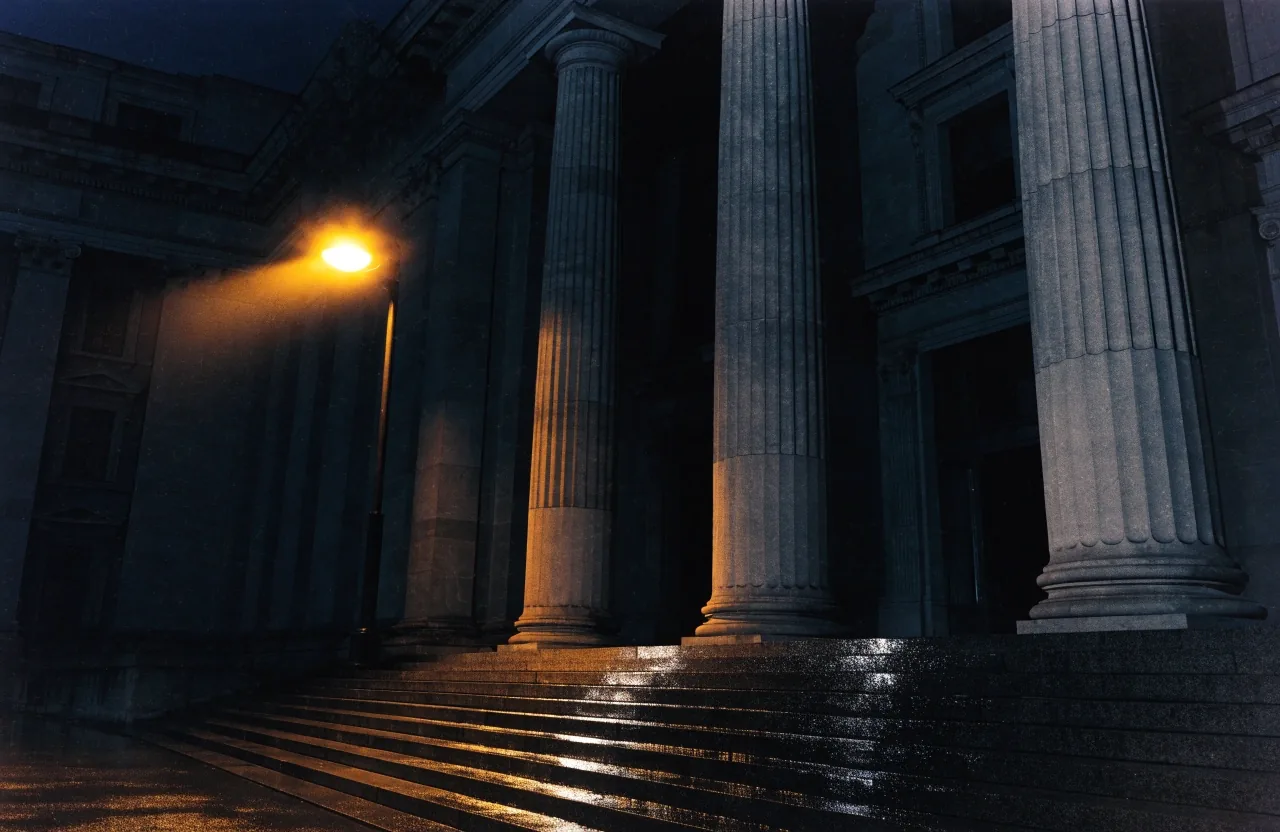 A courthouse facade under a single streetlight at night, wet stone steps