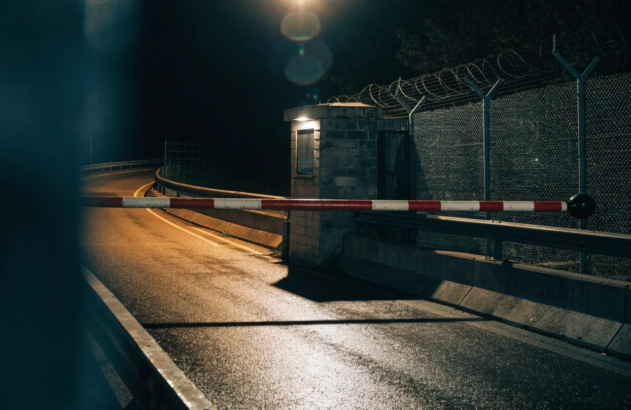 Rain-slicked European boulevard at midnight under one hard sodium streetlight