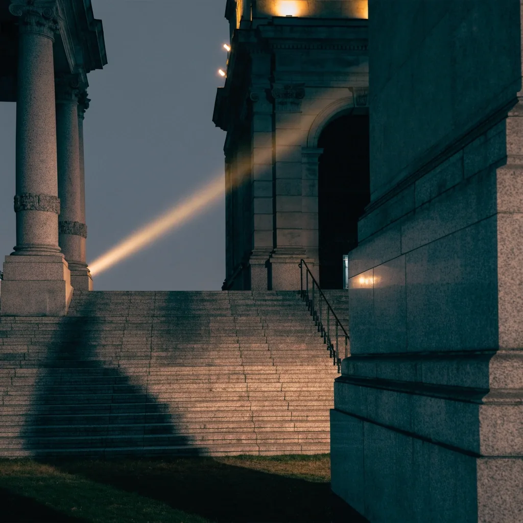 A floodlit stone colonnade of a government building at night with hard shadows between pillars